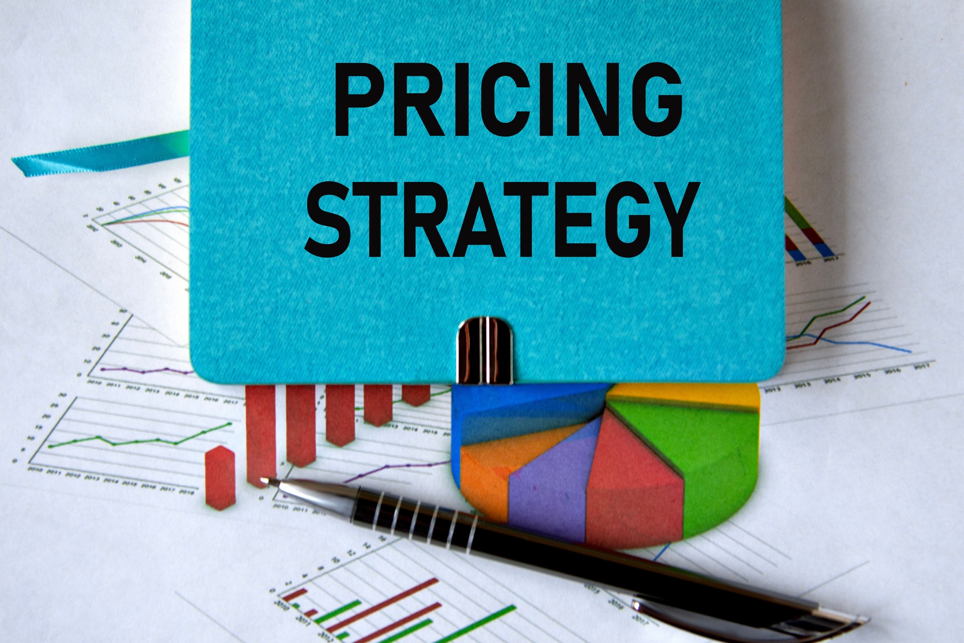 PRICING STRATEGY - words on a green piece of paper on the background of a chart and a pen